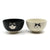 Two porcelain bowls, one black and one white with a smiling cat head illustration on them. Sat on a white background.