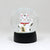 A white maneki-neko lucky cat snow globe figurine with a black base, featuring a waving lucky cat holding a gold sign and wearing a red collar, set against a plain light gray background.