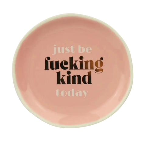 A round ceramic plate in a soft pink color with the phrase 'just be fucking kind today' printed on the inside. The words 'just be' and 'today' are in a light beige text, while 'fucking kind' is in a bold gold text.