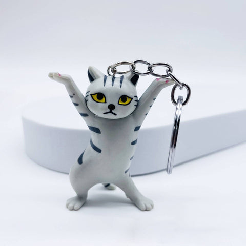 A white and gray tabby cat keychain figurine with yellow eyes and black stripes, posed with its paws raised, attached to a silver metal key ring on a clean white background.