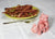 Two pink ceramic pig-shaped salt and pepper shakers on a white tablecloth with a plate of bacon in the background.