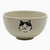 An off-white ceramic bowl with black speckles and a black cat face illustration on the front, set against a plain white background.