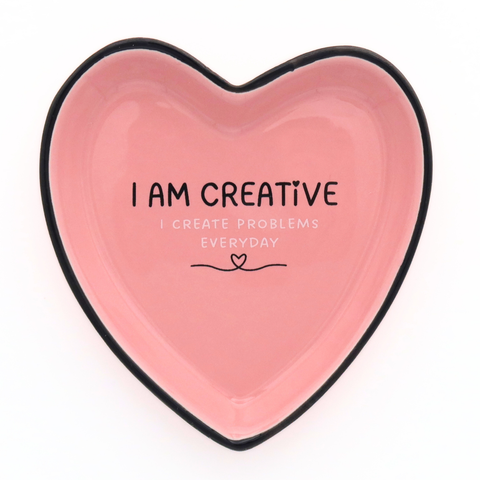 Heart-shaped pink plate with black rim and text 'I AM CREATIVE I CREATE PROBLEMS EVERYDAY' on a white background.