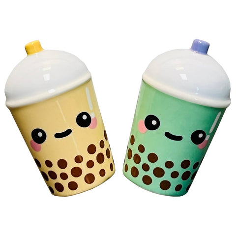 Two cute ceramic boba tea cup containers with smiling faces, one in pale yellow and one in mint green, both with brown boba and white lids.
