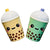 Two cute ceramic boba tea cup containers with smiling faces, one in pale yellow and one in mint green, both with brown boba and white lids.