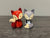 Two ceramic fox figurines, one red and one gray, on a wooden surface.