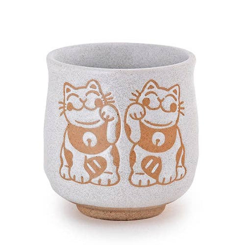 A Yunomi style tea cup with two japanese lucky cats side by side waving on a white background.