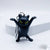 A black cat keychain figurine with raised paws and bright yellow eyes, attached to silver metal key rings, photographed on a clean white surface with a white display block in the background.