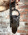Hand holding a necklace with a large, dark stone pendant against a brick wall.