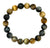 A beaded stretch bracelet made of polished round gemstone beads in alternating dark gray, black, brown, and golden-yellow hues, arranged in a circle on a plain white background.
