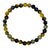 A beaded stretch bracelet made of polished round gemstone beads in earthy olive green, brown, black, and golden yellow tones, arranged in a circle on a plain white background.