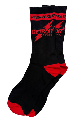 A pair of black crew socks with red accents, featuring the red text 'NEVER FAKE IT TAKE IT' and 'DETROIT ORIGINAL' with red lightning bolts on the upper leg, shown against a plain white background.